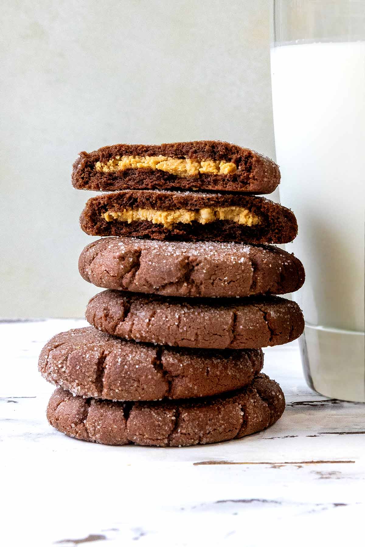 Chocolate peanut butter cookies in a stack, the top one broken in half, on a worn white background.