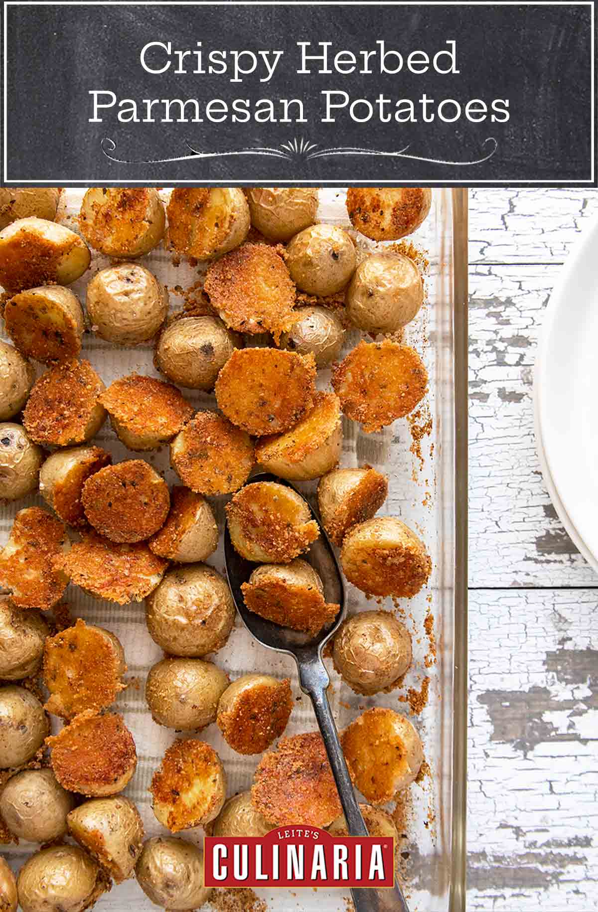 Crispy Parmesan potatoes in a glass baking dish on a white wooden background.