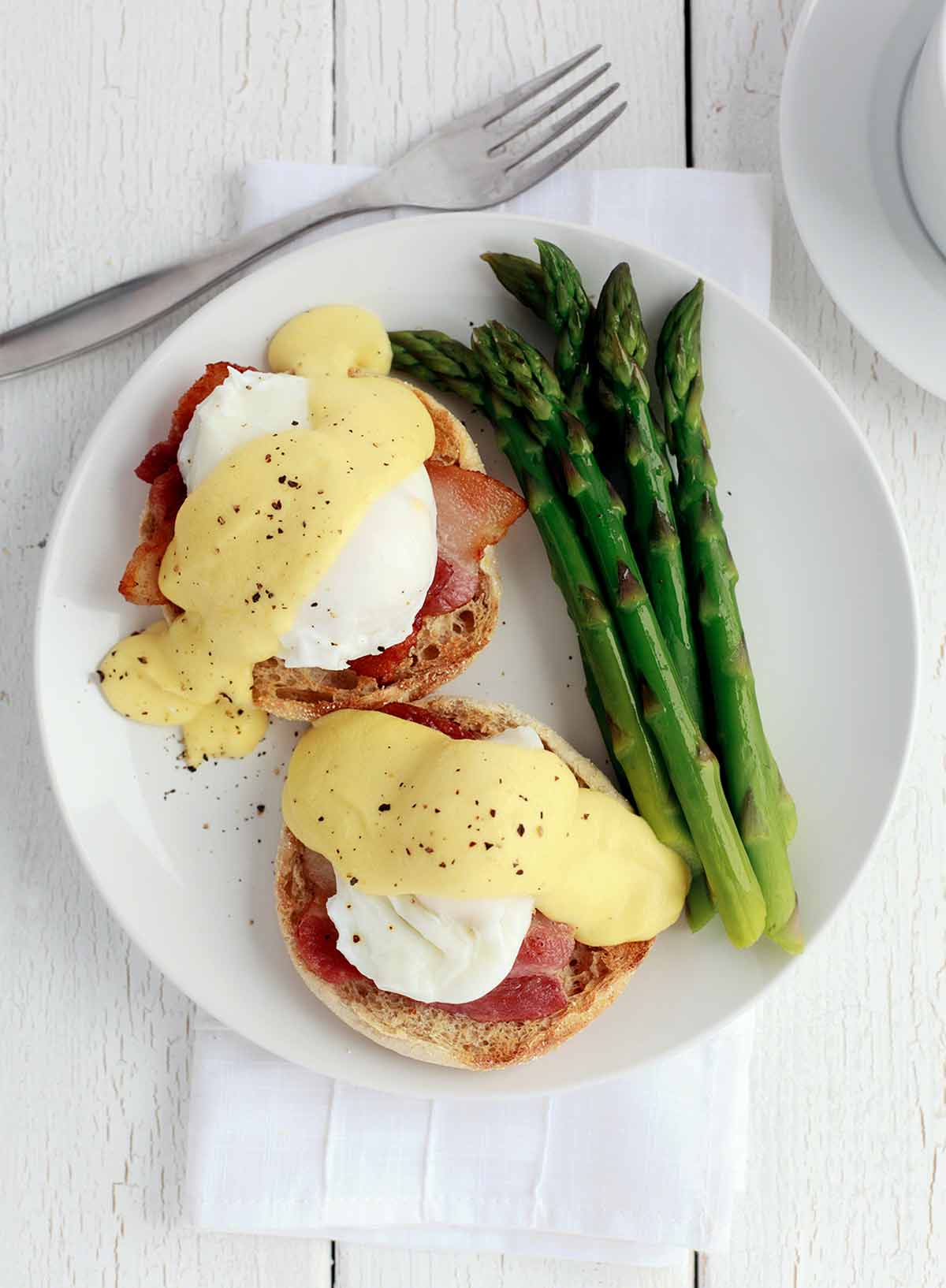 Two Julia Child's eggs Benedict on a white plate with a side of asparagus.