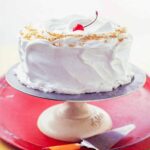 A Lady Baltimore cake covered with billowy white frosting on cake stand.