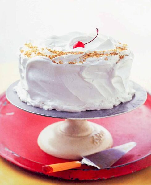 A Lady Baltimore cake covered with billowy white frosting on cake stand.