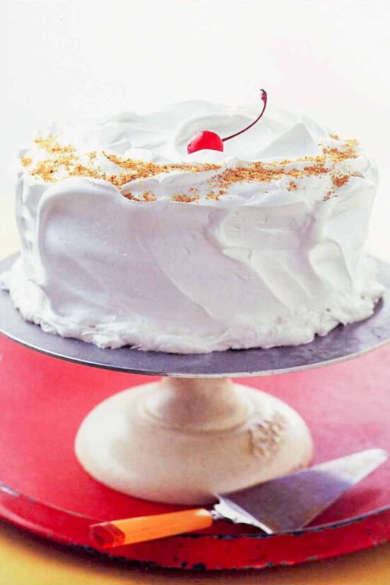 A Lady Baltimore cake covered with billowy white frosting on cake stand.