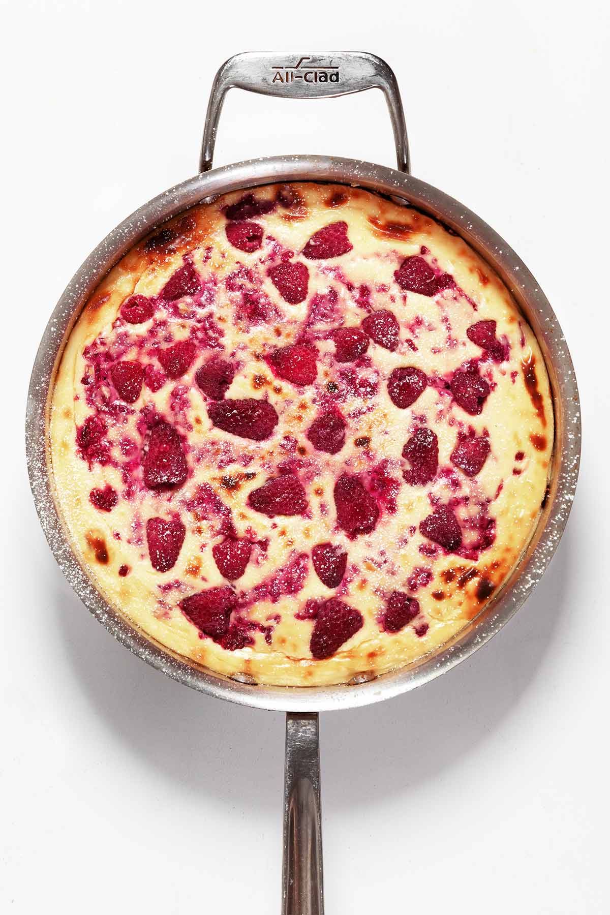 A baked lemon cheesecake topped with raspberries in a metal skillet.
