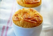 Two puffy, golden Parmesan and Gruyere Cheese Souffles in white bowls on a towel.