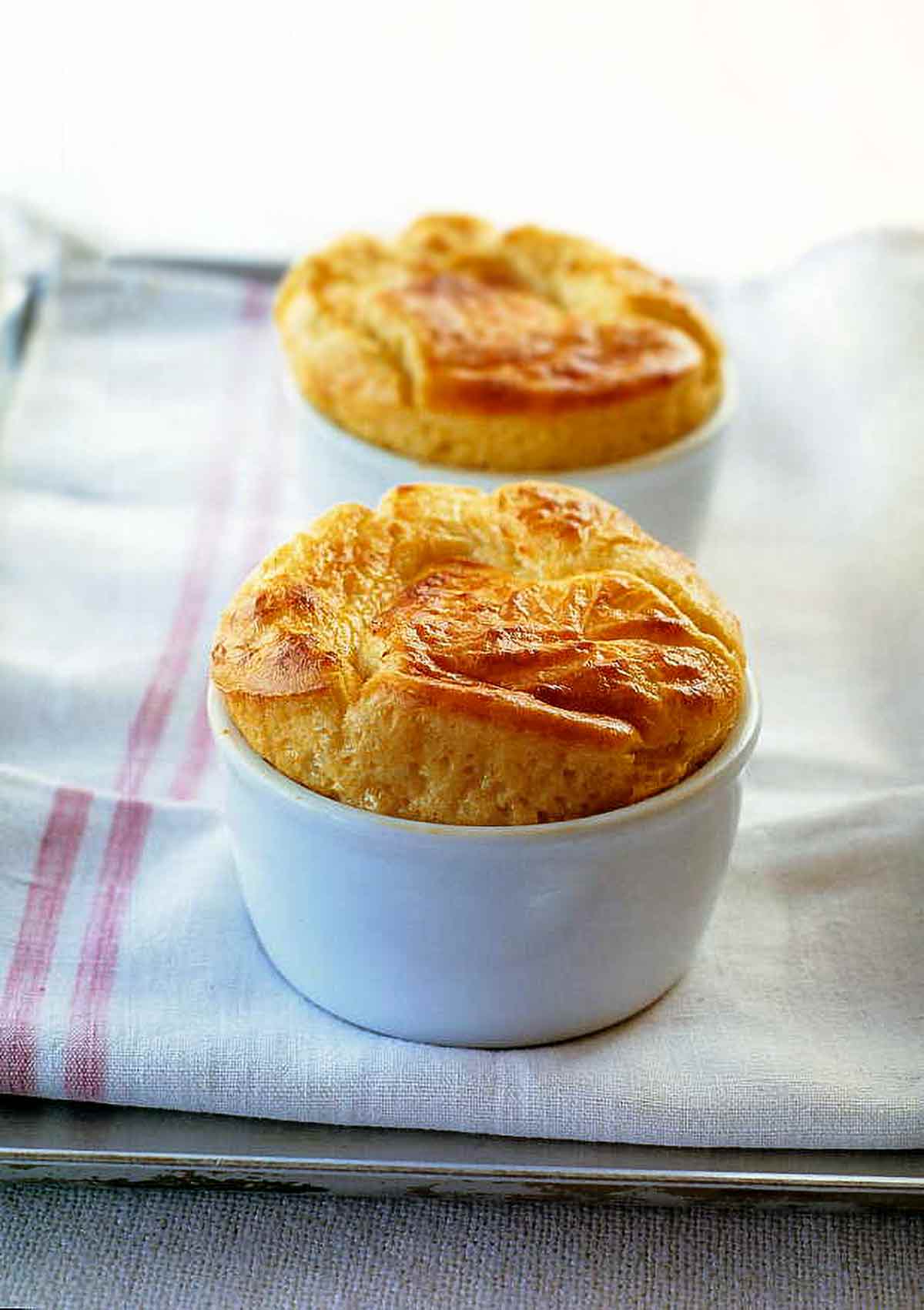 Two puffy, golden Parmesan and Gruyere Cheese Souffles in white bowls on a towel.