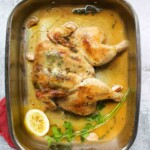A spatchcocked roast chicken in a metal roasting pan with a half lemon and some fresh parsley.