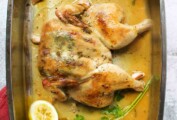 A spatchcocked roast chicken in a metal roasting pan with a half lemon and some fresh parsley.