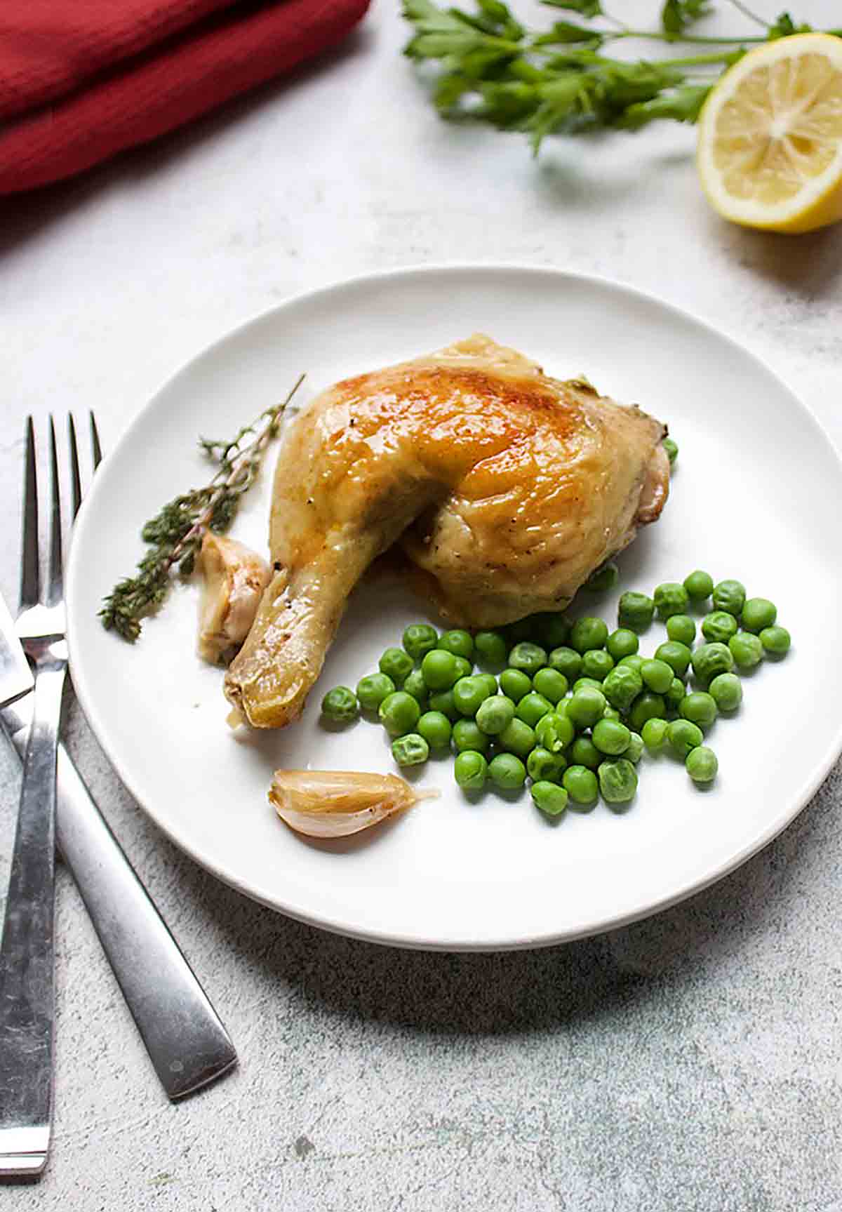 A roast chicken leg on a white plate with peas, thyme and garlic.