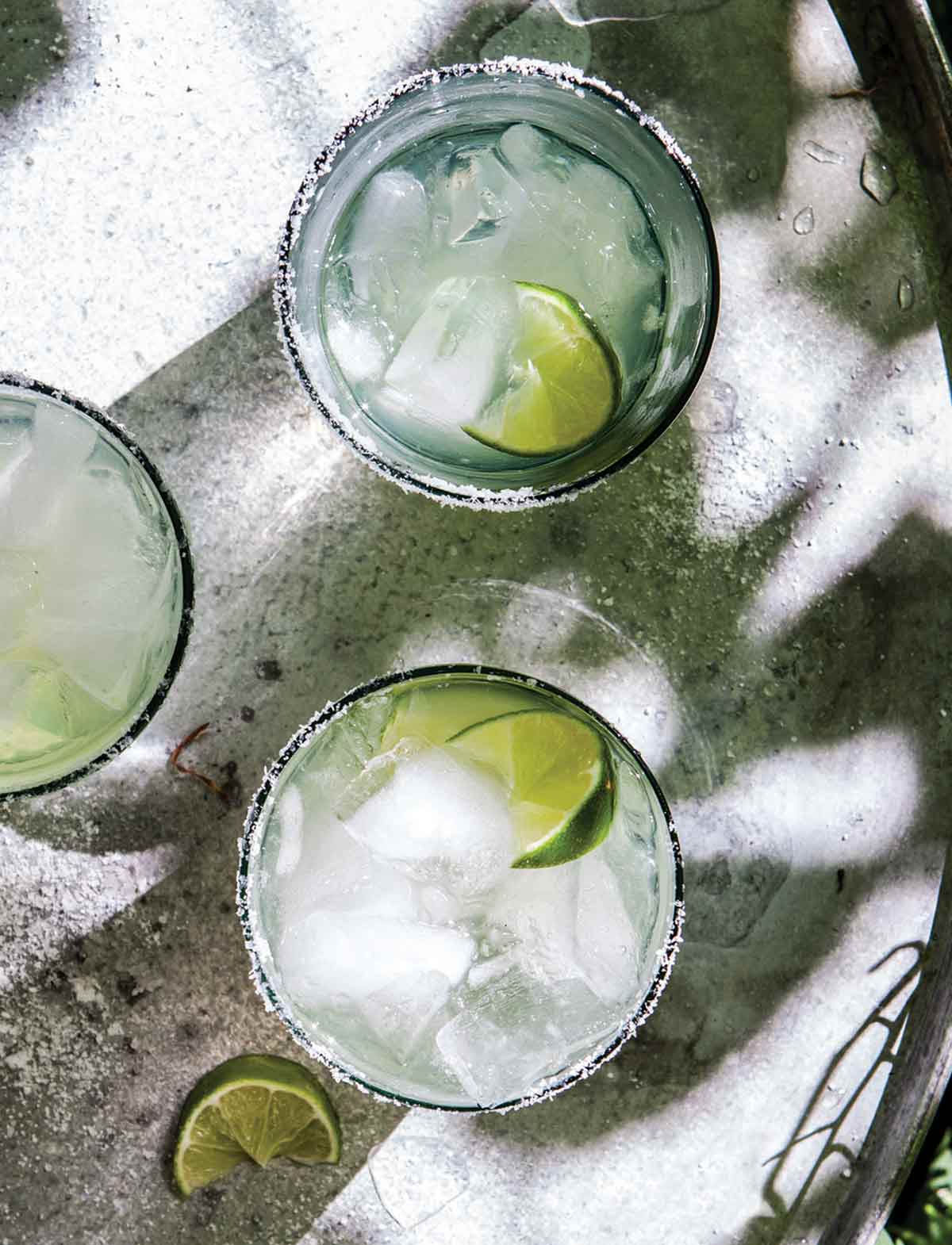 Three glasses of ultimate margarita with lime wedges.