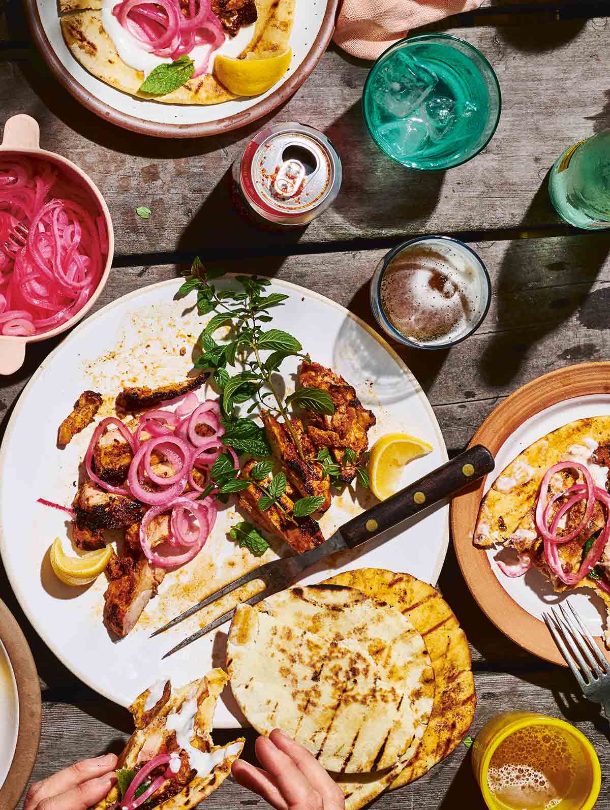 Grilled chicken thighs on plates with pickled onions, fresh herbs, and grilled flat bread.