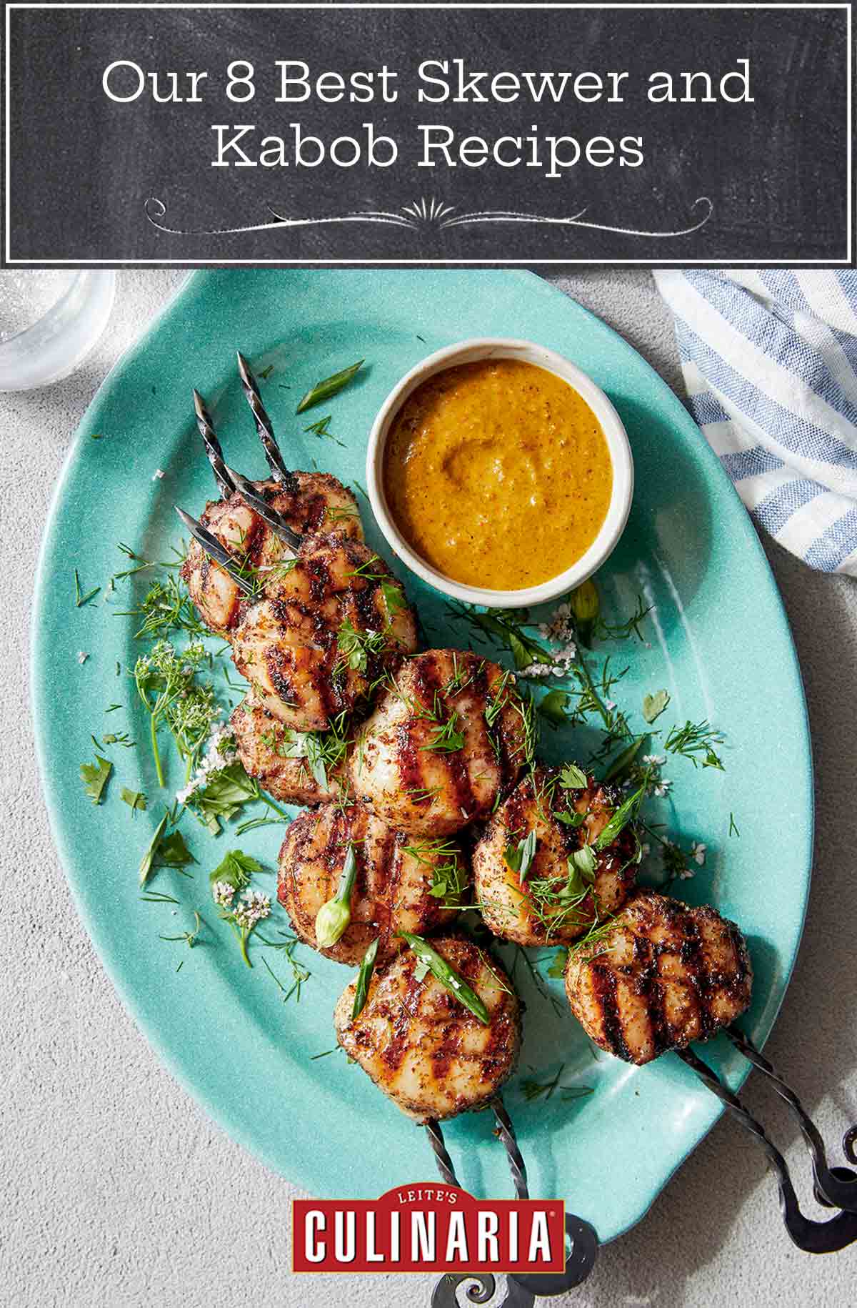 Two skewers of grilled scallops on a aqua platter with a small bowl of sauce on the side.