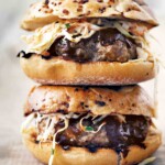Two barbecue pork burgers with slaw and barbecue sauce stacked on top of each other.