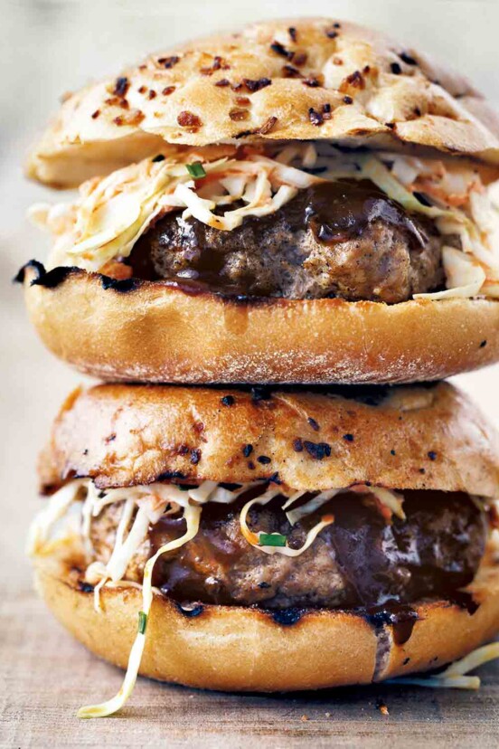 Two barbecue pork burgers with slaw and barbecue sauce stacked on top of each other.