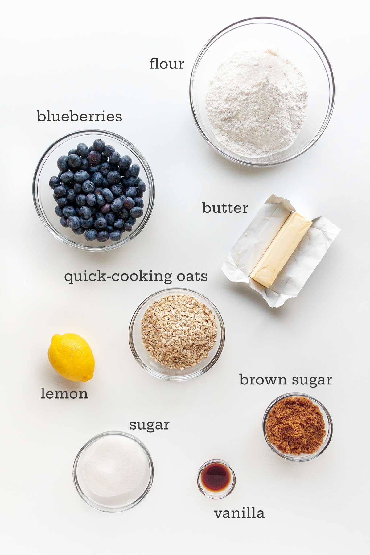 Ingredients for blueberry crumble--blueberries, flour, butter, oats, lemon, white and brown sugars, and vanilla.