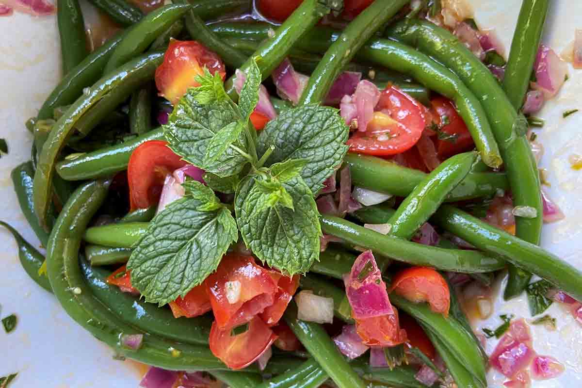 A white plate topped with green beans, diced tomatoes, red onion, and fresh mint.