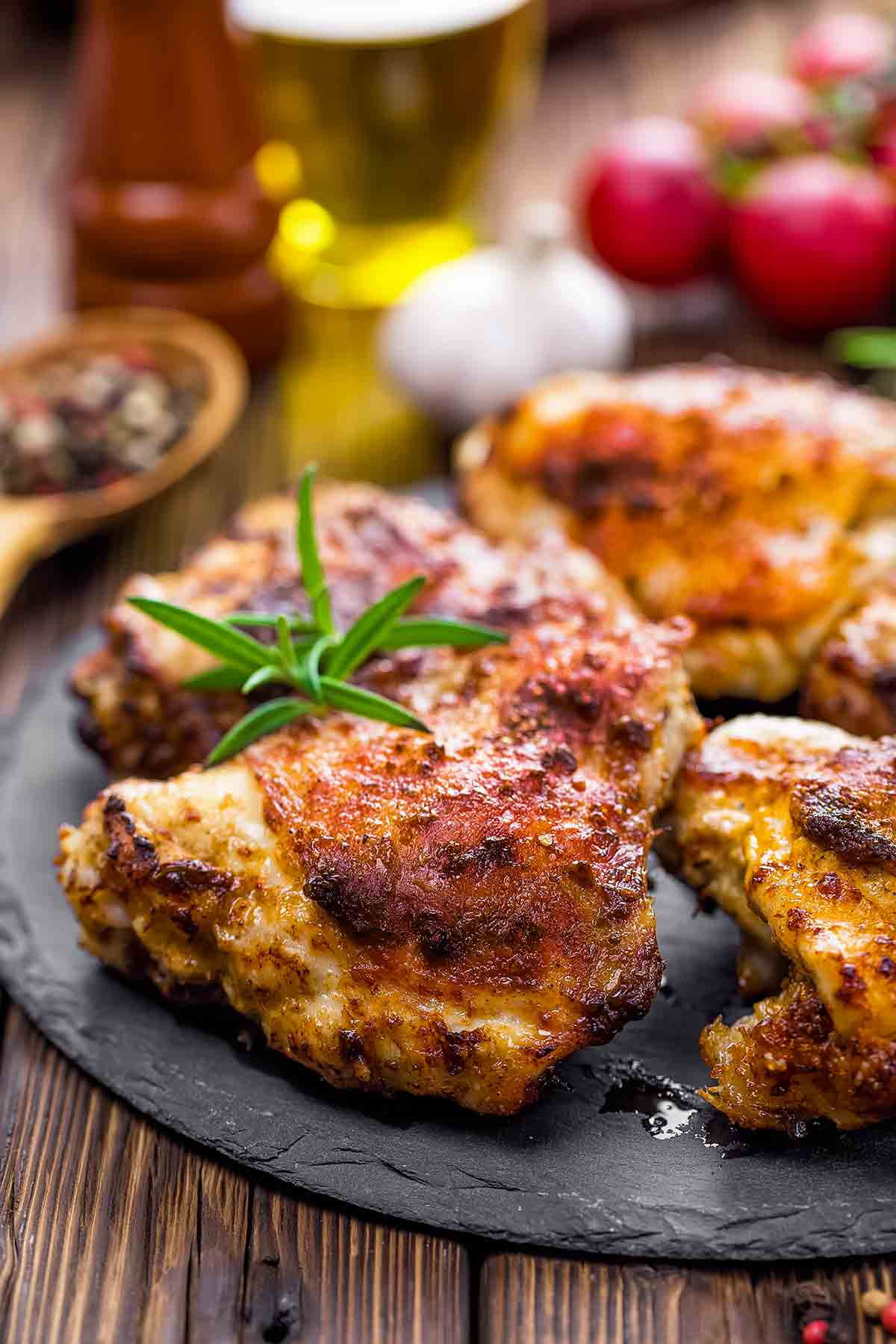 Grilled chicken thighs on a platter with a sprig of rosemary on top.