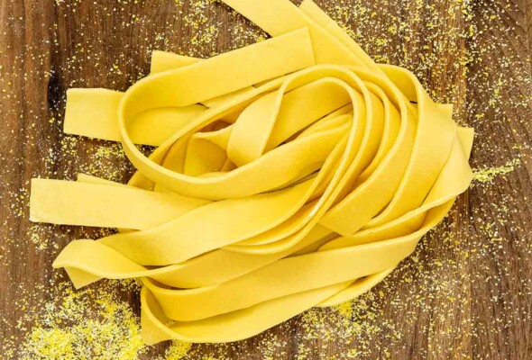 A tangle of fresh pasta noodles on a cutting board that is sprinkled with semolina.