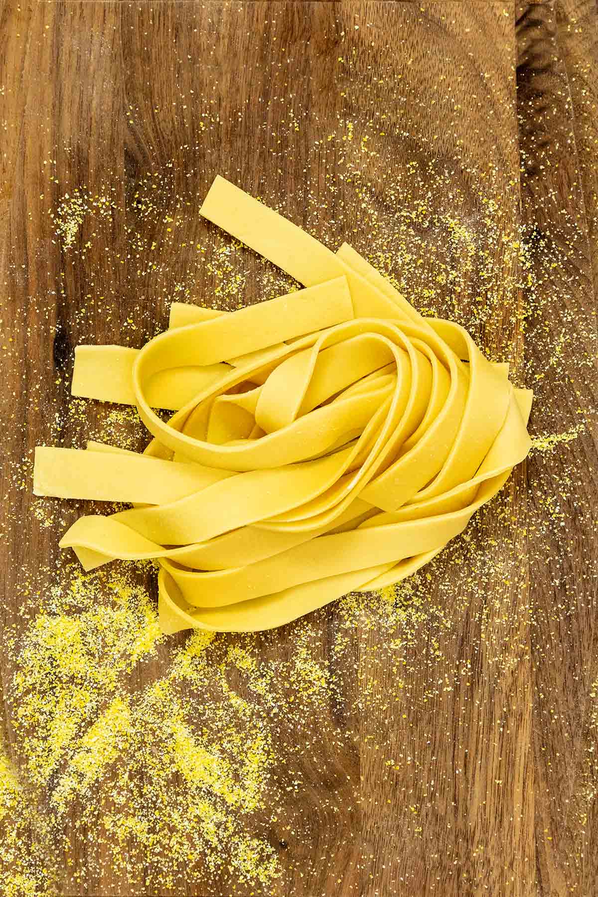 A tangle of fresh pasta noodles on a cutting board that is sprinkled with semolina.