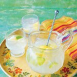 A pitcher and two glasses of limeade on a colorful platter with a linen napkin on the side.