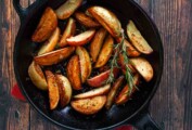 A cast-iron skillet filled with roasted grilled potatoes and two sprigs of rosemary on a wooden table.