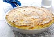 A skillet lemon souffle made entirely in a frying pan, sitting on a wire rack, blue cloth wrapped around the handle.