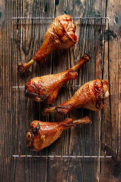 Four smoked turkey legs on a wire rack on a wooden table.