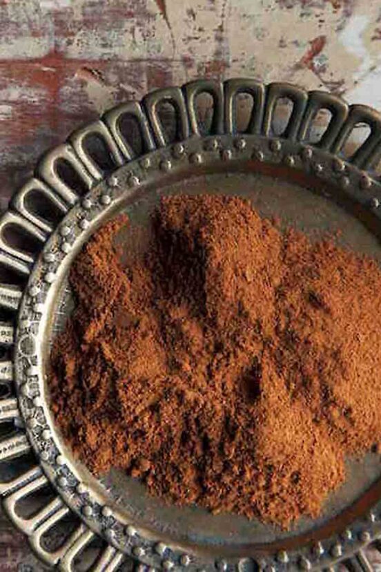 A pile of ground cinnamon on a decorative metal plate.