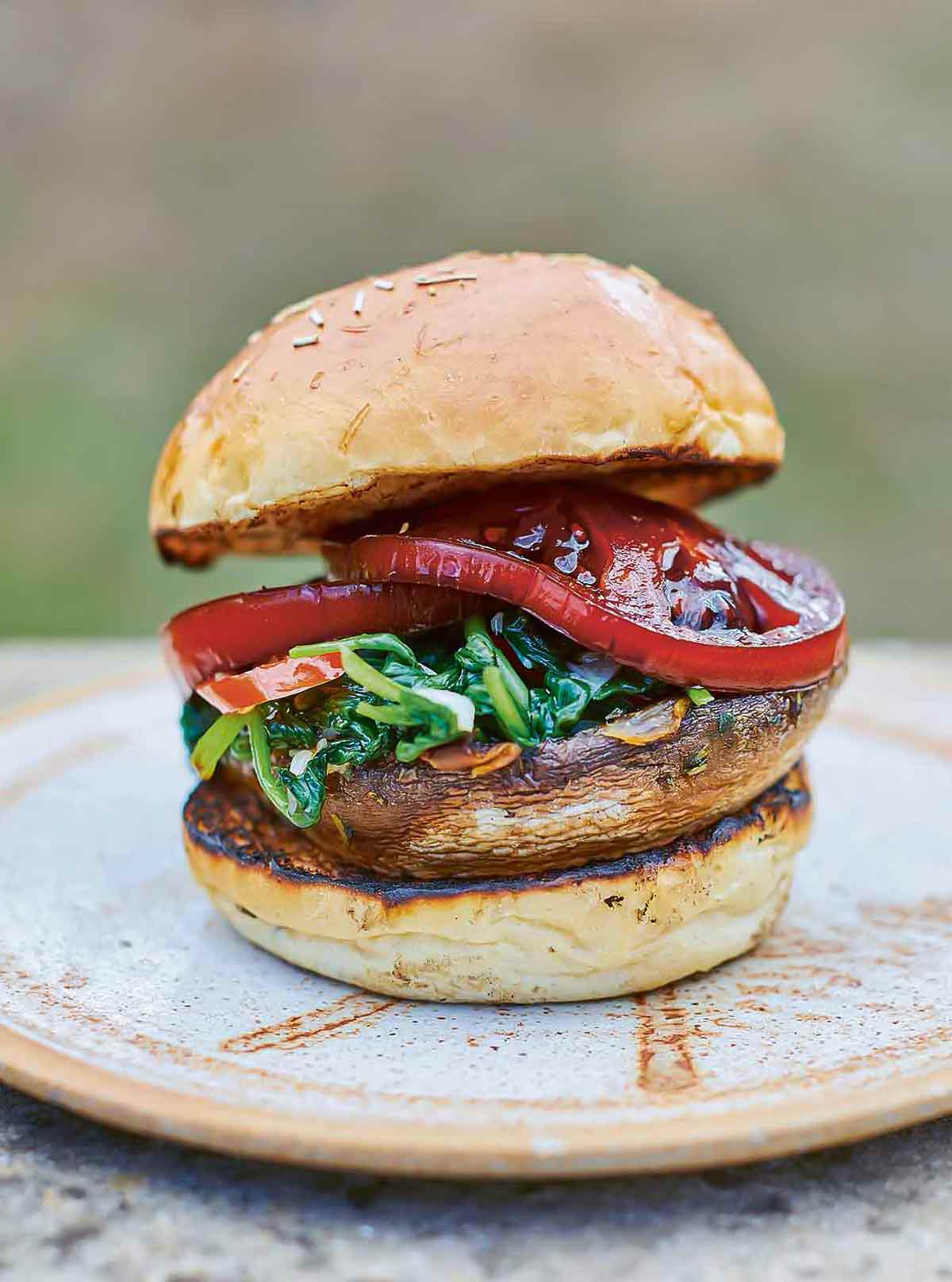 A spinach, tomato, and mushroom burger on a grilled bun.