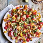 A white plate filled with charred corn salad and a halved lime and bowl of dressing on the side.