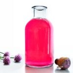 An apothecary jar of magenta-pink chive blossom vinegar; a cork and chive blossoms rest nearby.