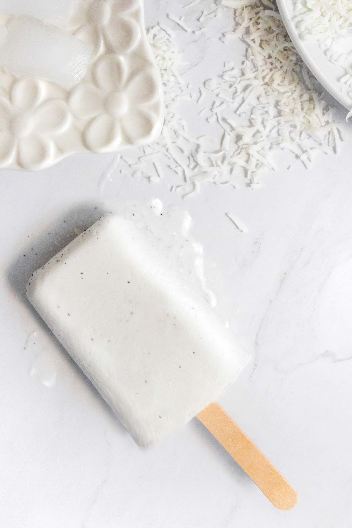 A coconut milk popsicle on a marble slab.