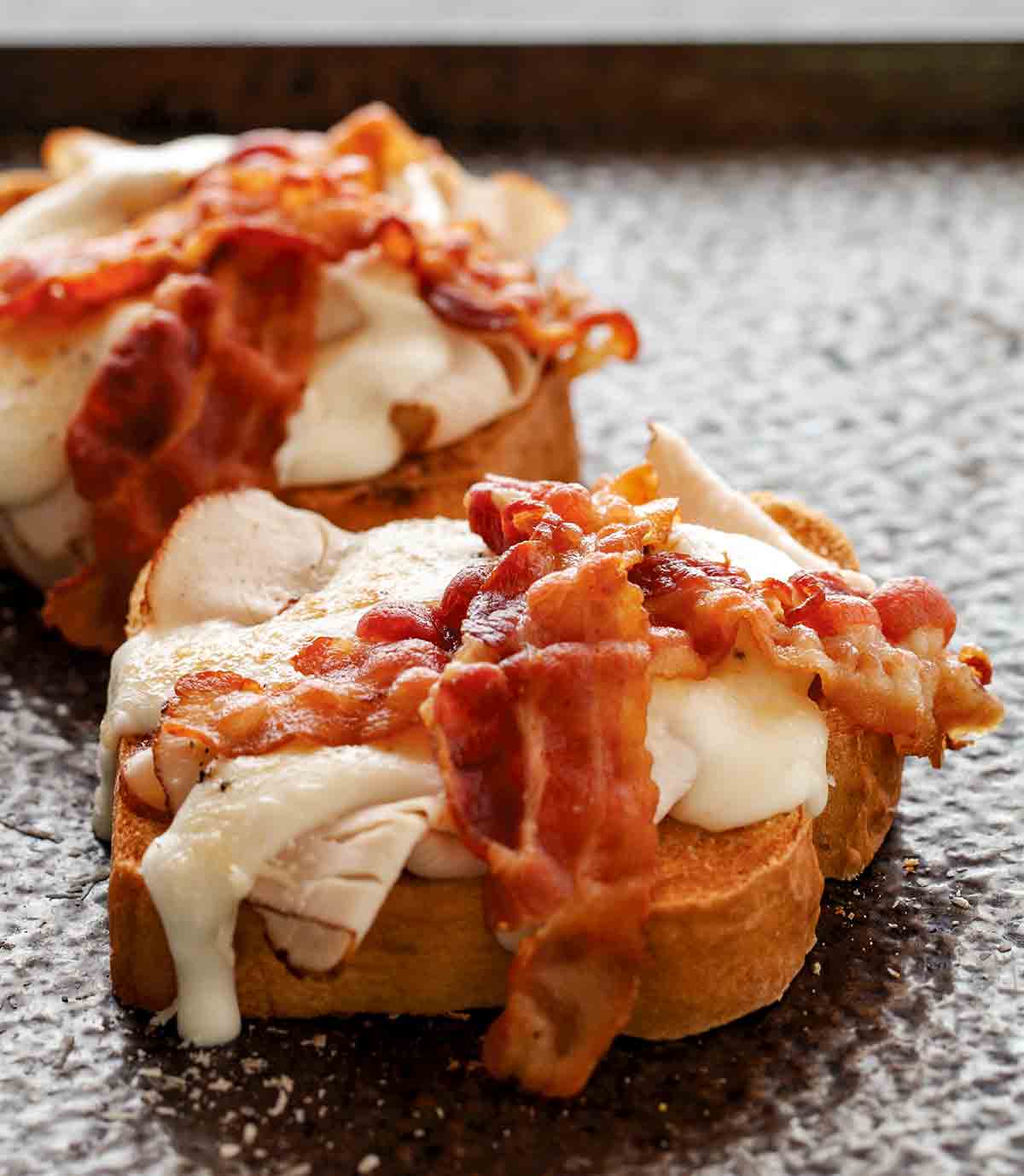Two slices of toast, each topped with sliced turkey, melted cheese, and two slices of bacon.