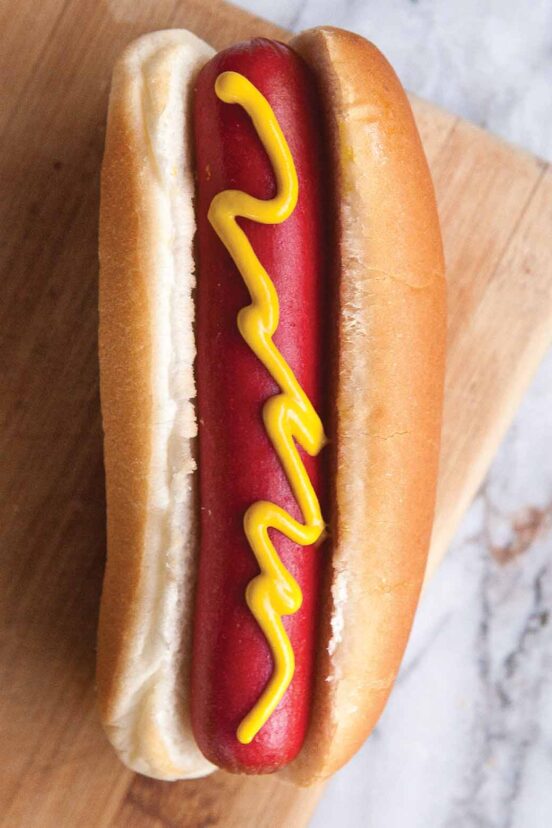 A hot dog on a bun with a squiggle of mustard.