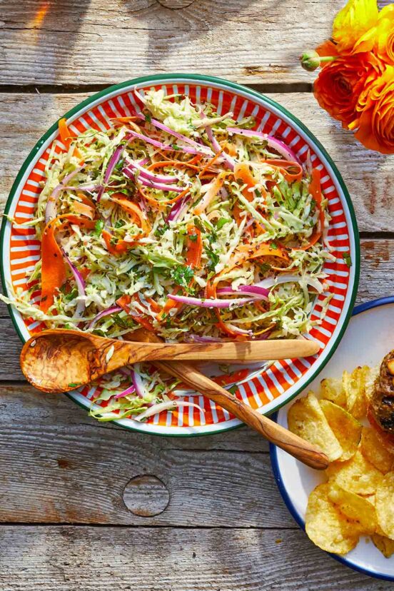 A bowl filled with coleslaw with wooden serving utensils resting on top.