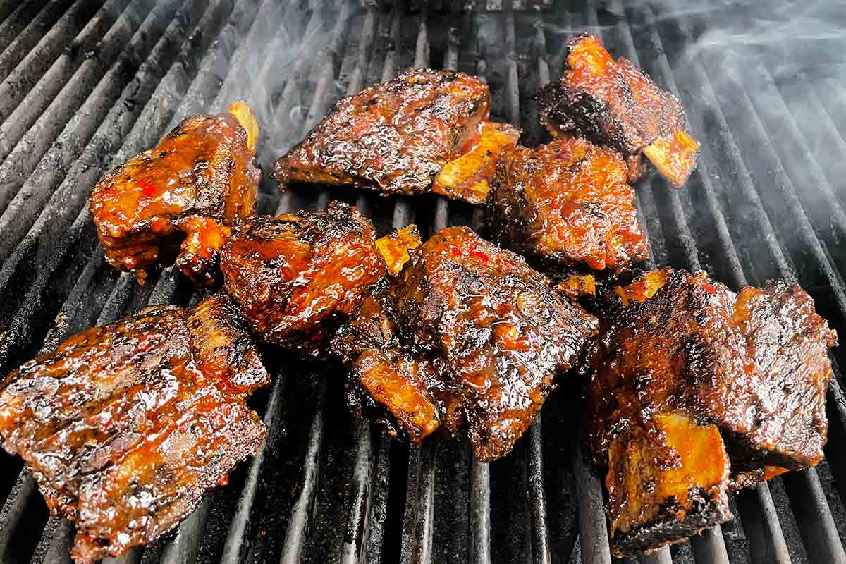 Several grilled beef short ribs, coated with bbq sauce on a grill.
