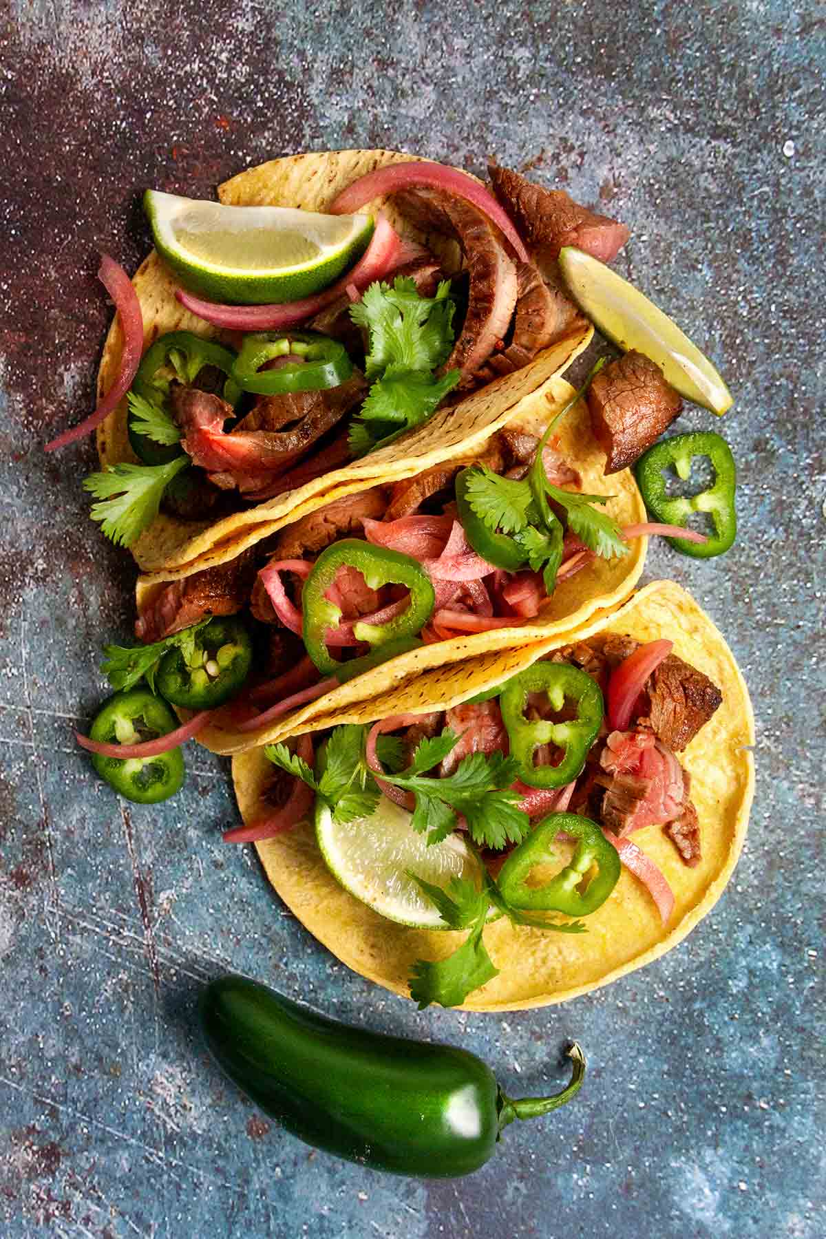 Three skirt steak tacos filled with sliced steak, jalapeño, pickled onion, lime, and cilantro.