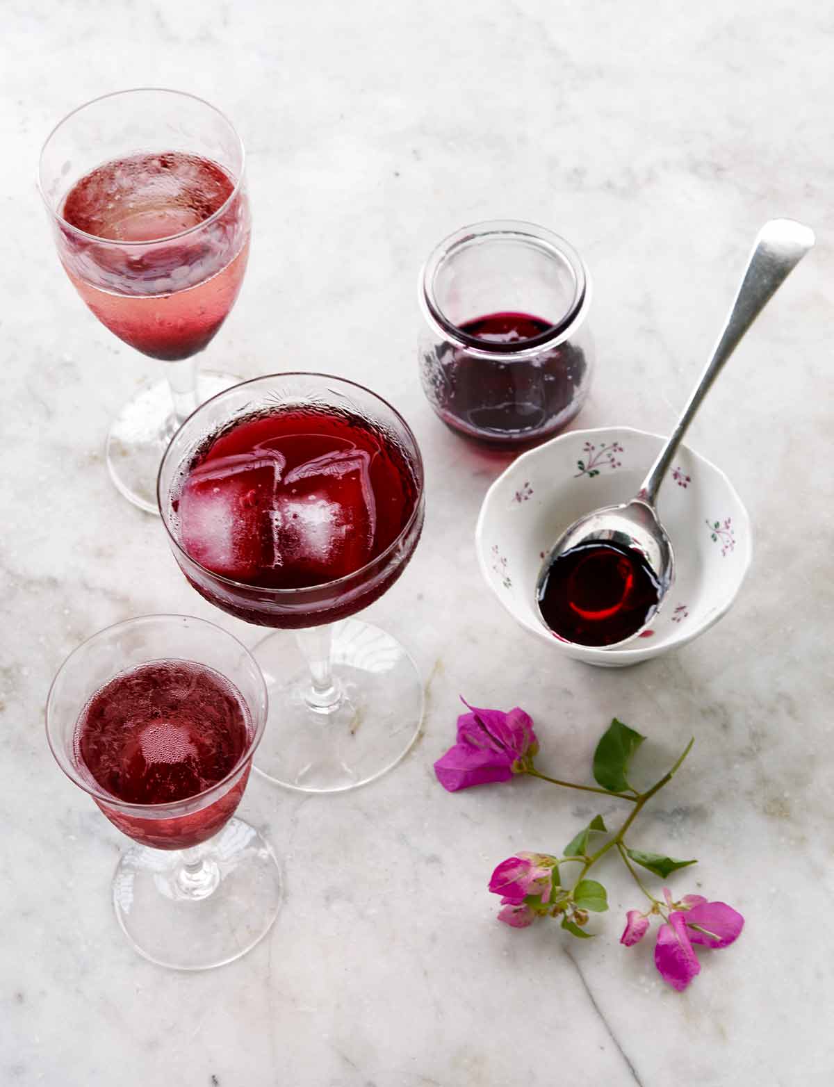 Four glasses filled with hibiscus cocktail, with a hibiscus flour and a dish with a spoon on the side.