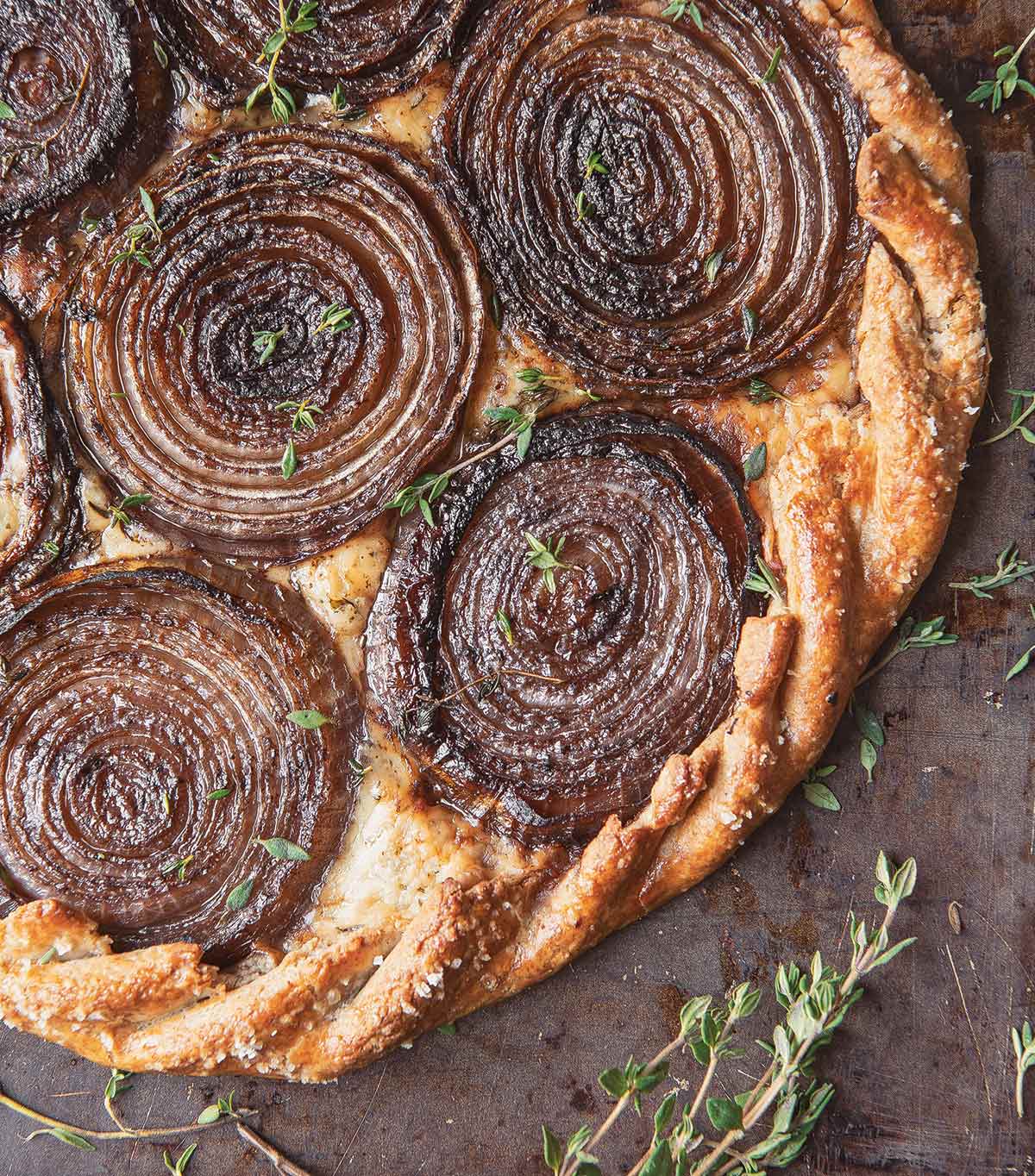 A tart with rounds of caramelized red onion and thyme leaves scattered around.