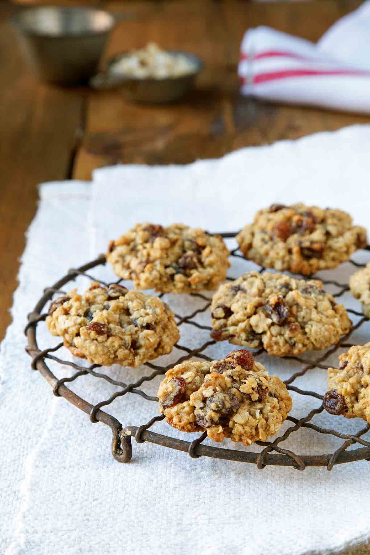 Seven oatmeal raisin cookies on a wire rack set on a white woven placemat.