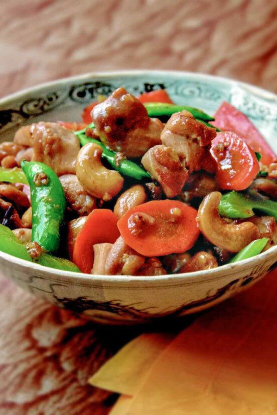 A bowl of cashew chicken with celery, carrots, and sugar snap peas.
