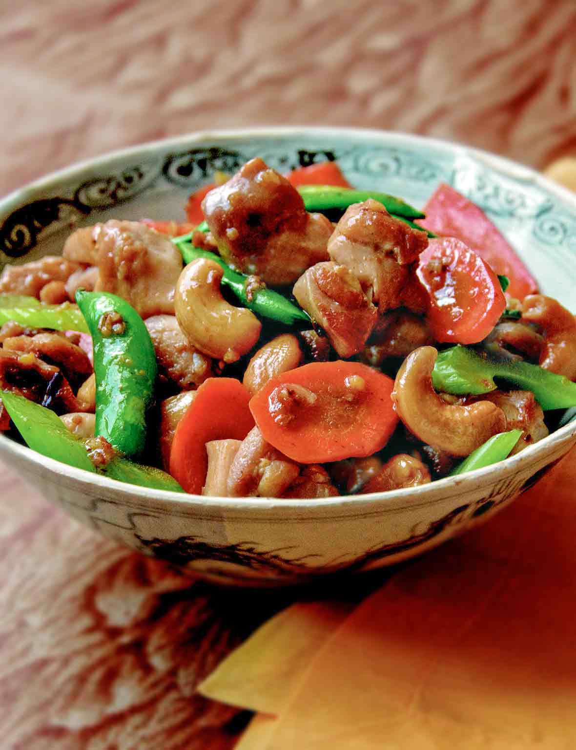 A bowl of cashew chicken with celery, carrots, and sugar snap peas.