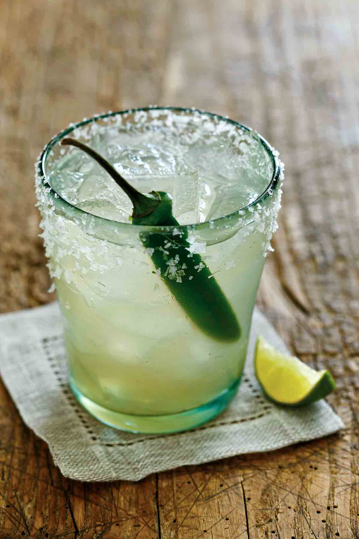A margarita in a short glass with a chile inside, salt on the rim, and a lime wedge on the side.