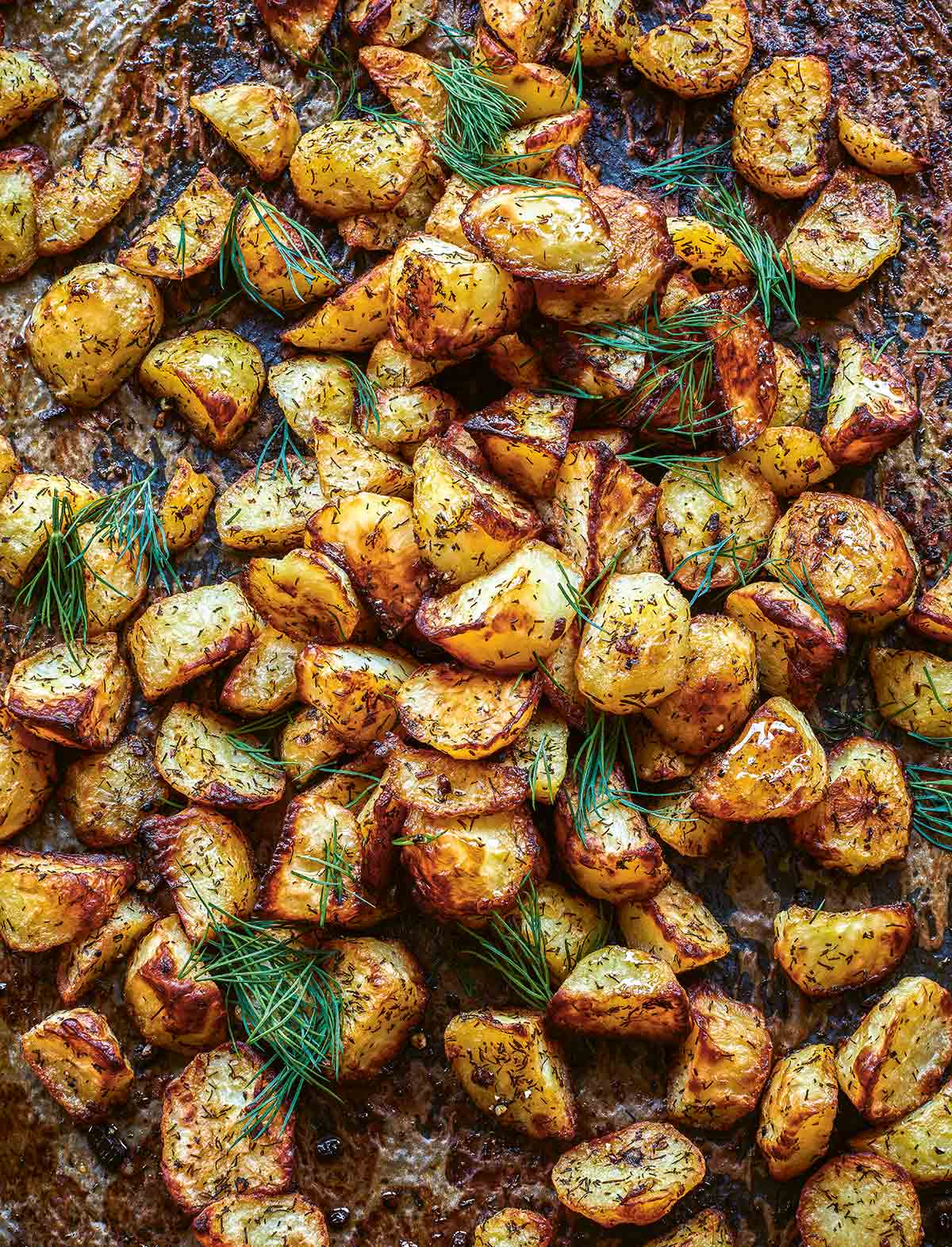 Roasted potatoes topped with dill on a baking sheet.