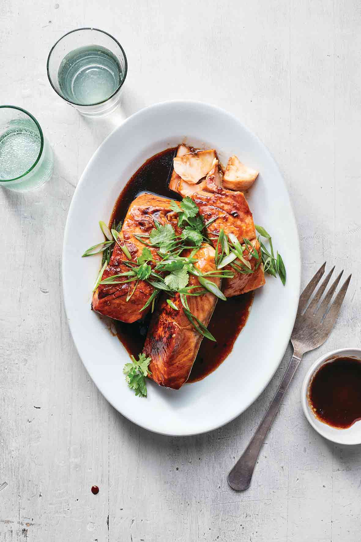 Three pieces of Vietnamese caramelized salmon on a white oval platter, topped with sliced scallions and cilantro.