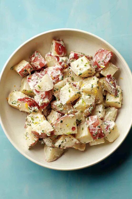 A white bowl filled with red potato salad with a creamy dressing.