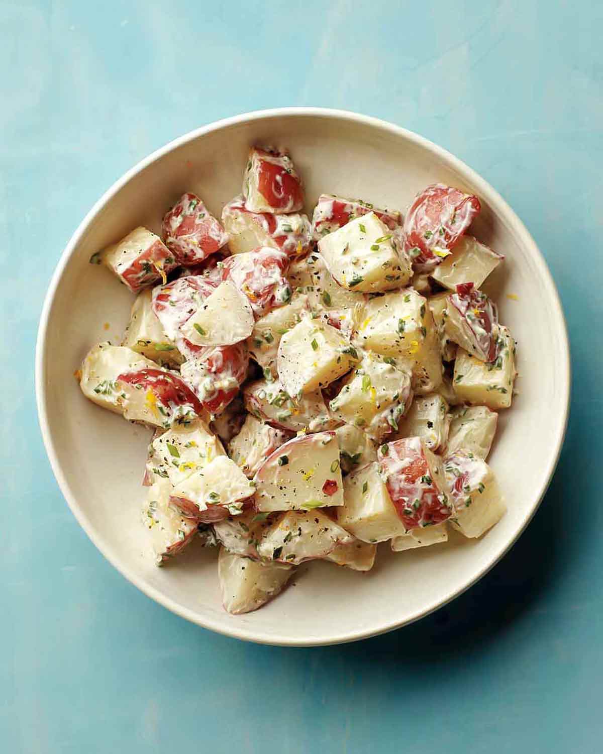 A white bowl filled with red potato salad with a creamy dressing.
