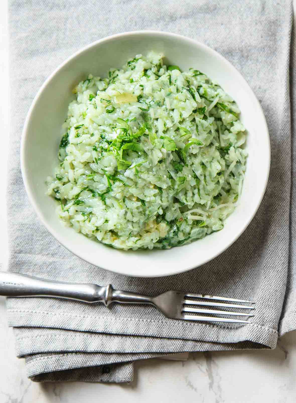 A bowl of spinach and arugula risotto on a grey napkin with a fork resting beside it.