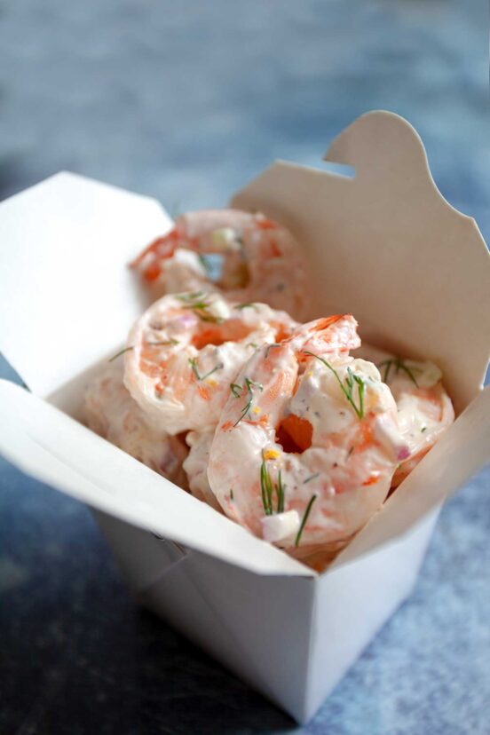 A white box filled with creamy shrimp and a little dill scattered on top.