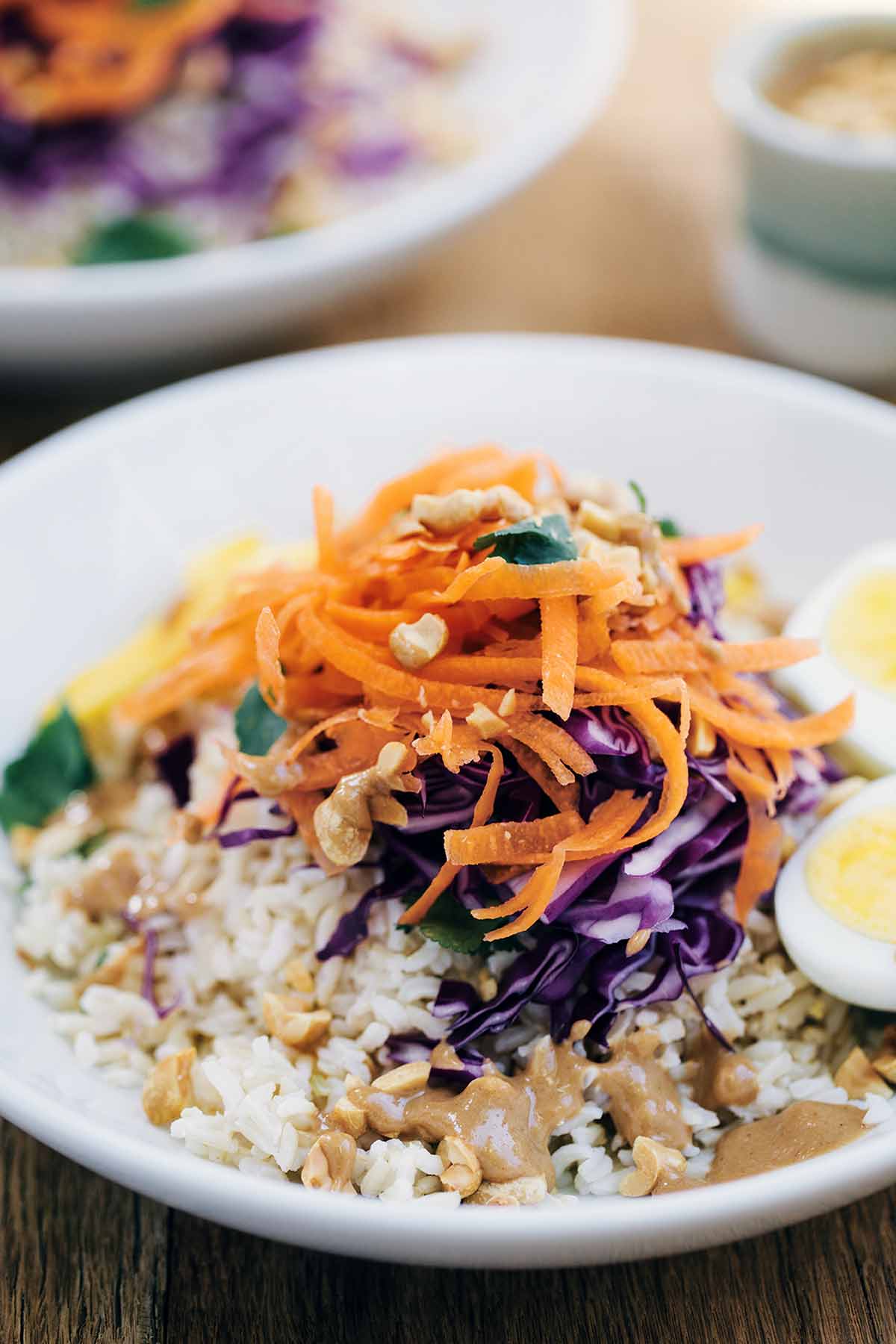 A bowl filled with gado gado salad withrice, peanuts, carrots, cabbage, and eggs.