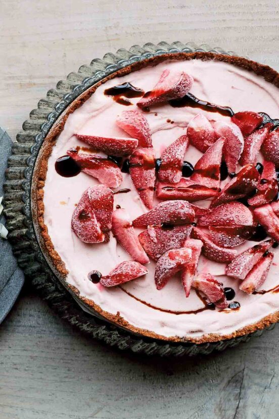 A whole strawberry ice cream pie drizzled with balsamic glaze in a fluted tart pan.